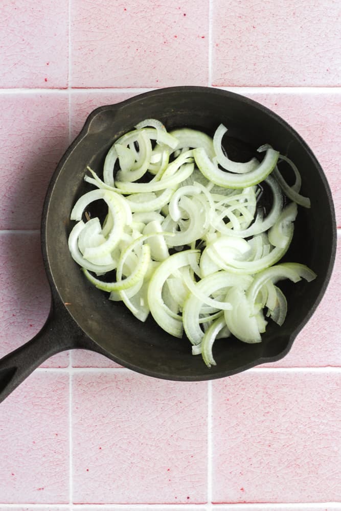 oil-free caramelized onions cooking in a cast iron pan photographed on a pink backdrop
