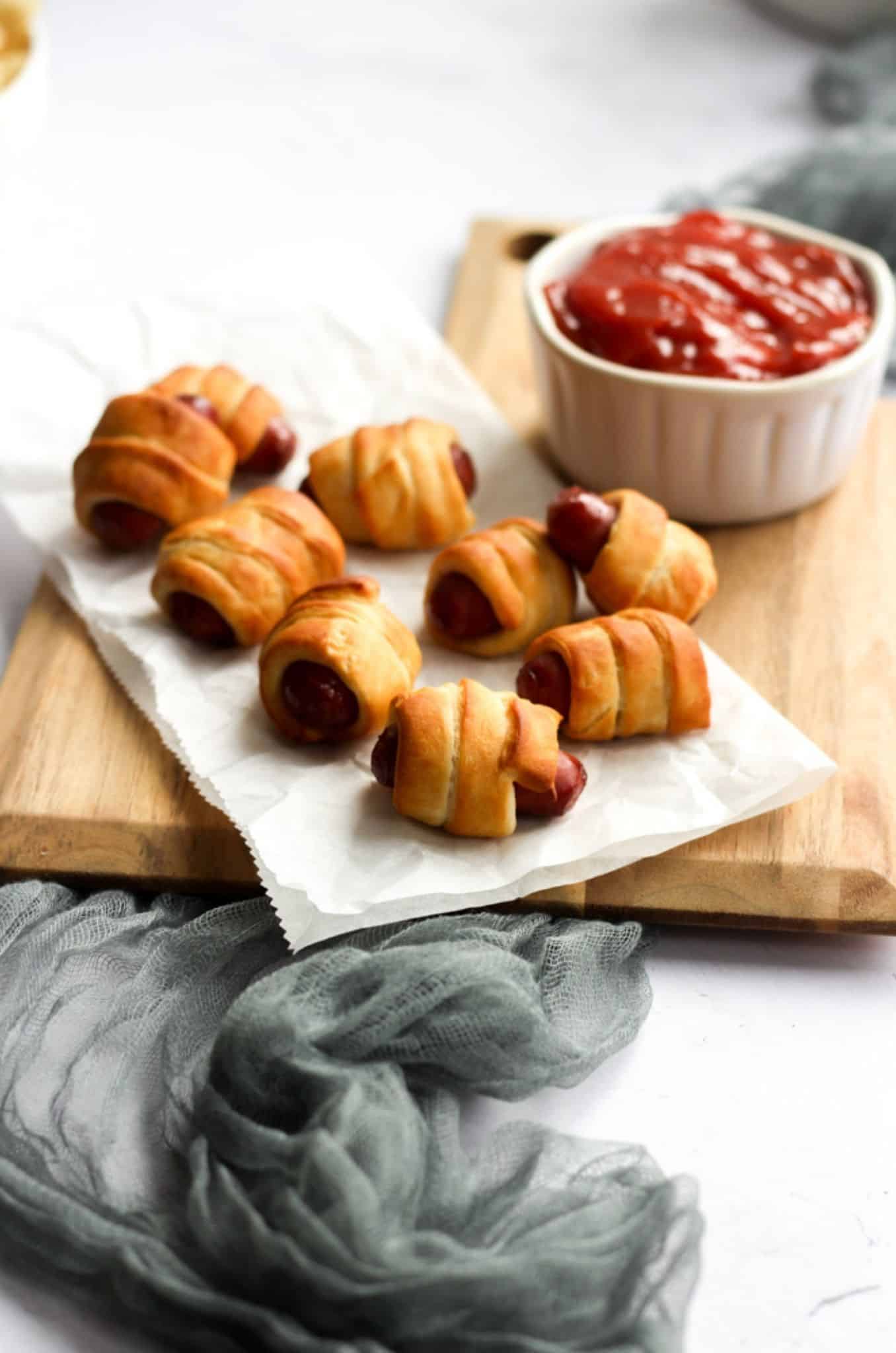 air fryer pigs in a blanket on parchment paper with a white bowl of ketchup