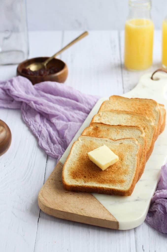 4 pieces of toast made in the air fryer displayed on a marble and wood cutting board. The board is sitting on top of a lilac colored linen napkin