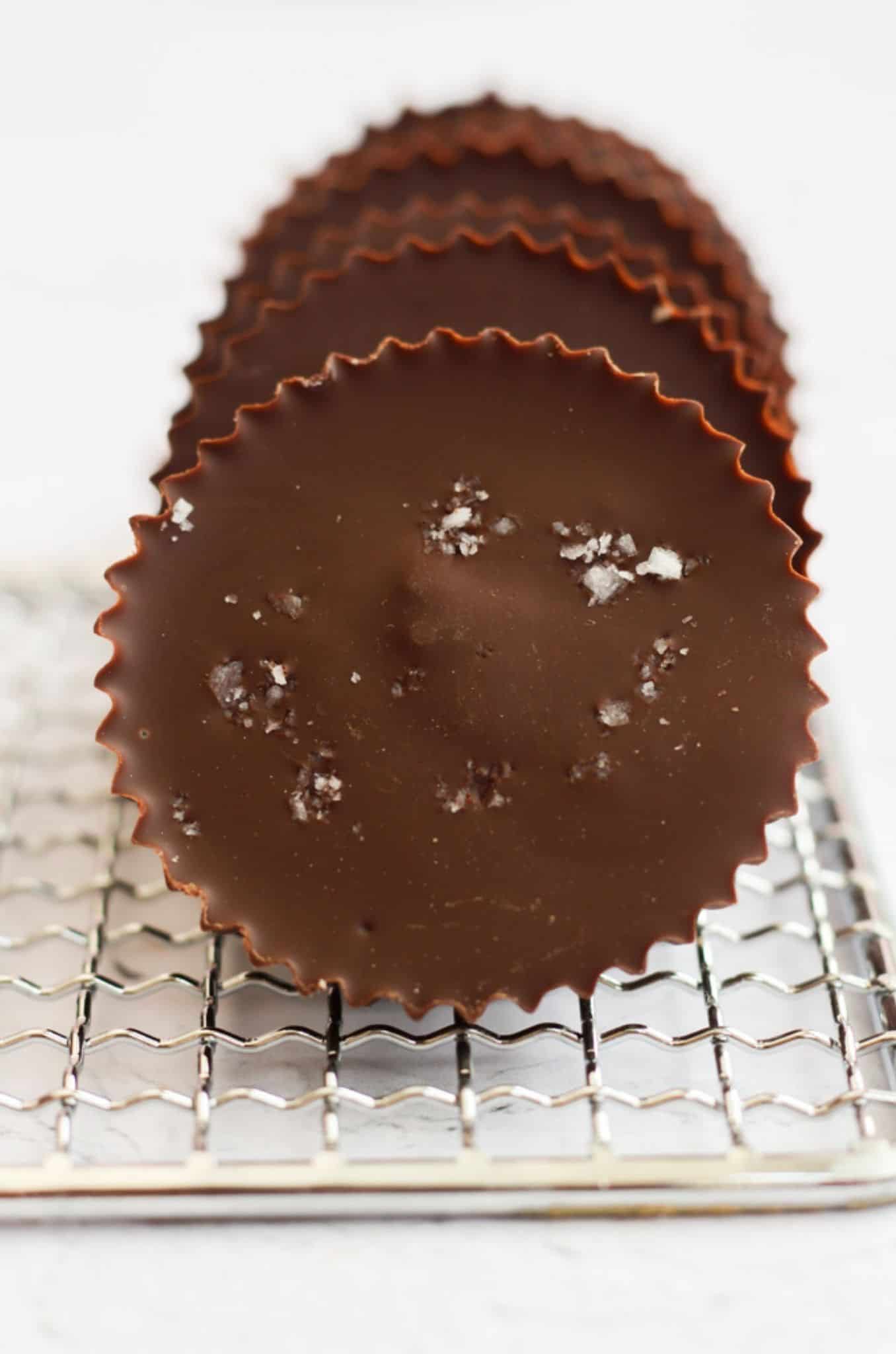 vegan almond butter cups lined up on a cooling rack, and the first one is sprinkled with sea salt