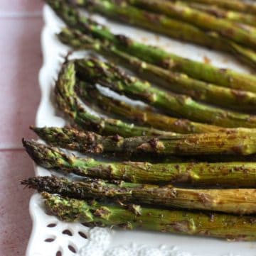 balsamic asparagus laid out on a white platter on a pink backdrop