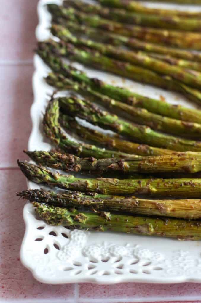 balsamic asparagus laid out on a white platter on a pink backdrop