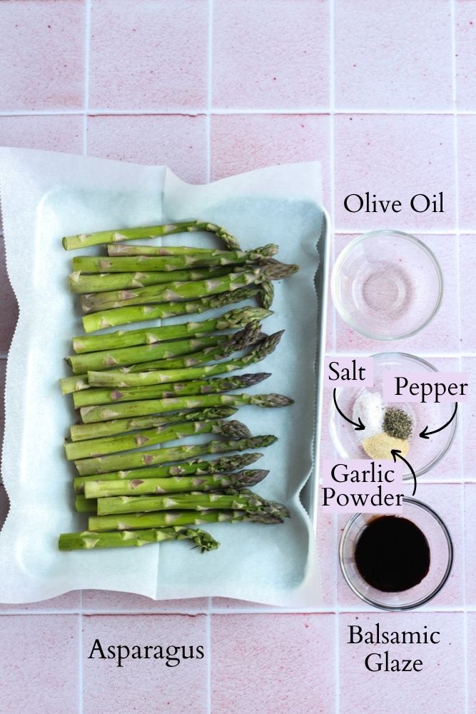 ingredients for balsamic asparagus in the air fryer on a pink tile backdrop labeled with black text