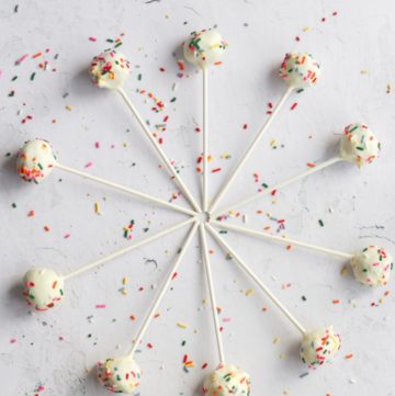 gluten free cake pops coated in white chocolate and sprinkles laying in a circle on a white backdrop