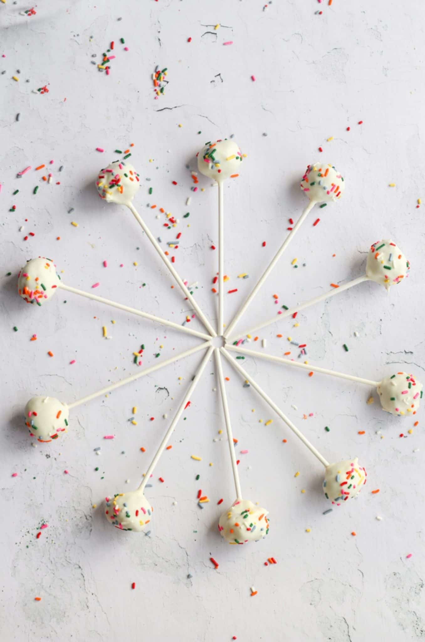 gluten free cake pops coated in white chocolate and sprinkles laying in a circle on a white backdrop