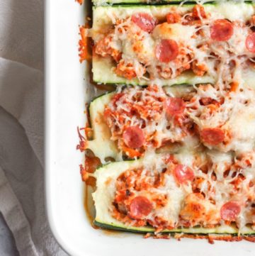 4 zucchini pizza boats in a white baking dish topped with melted cheese and mini pepperonis