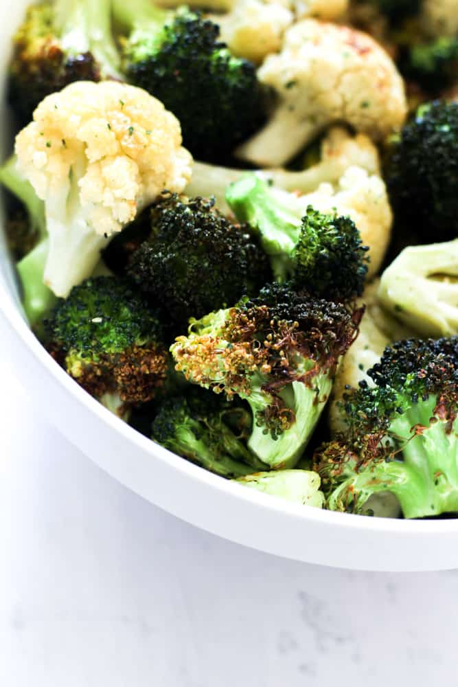 charred broccoli and cauliflower that was cooked in an air fryer in a white bowl on a gray backdrop