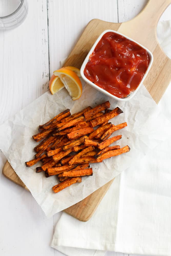 carrot fries on parchment paper on a wood baord with a bowl of ketchup