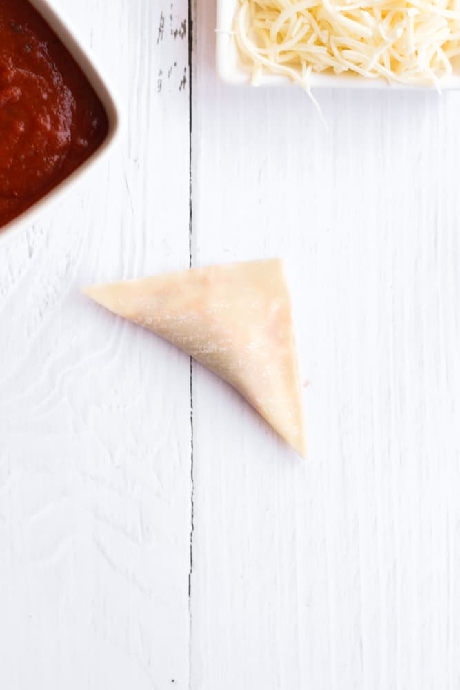 easy pizza roll using a wonton wrapper folded into a triangle on a white backdrop