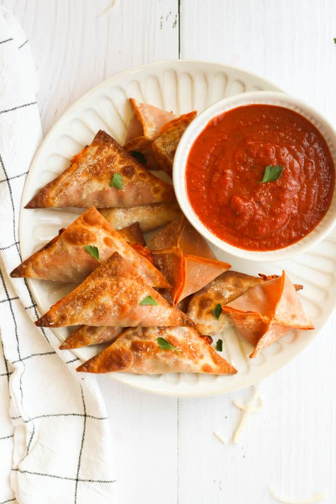 easy pizza rolls cooked in the air fryer on a white plate served with a side of pizza sauce on a white backdrop