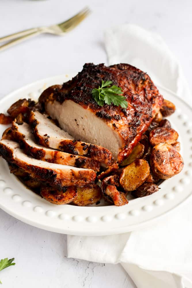 air fryer pork loin sliced on a white platter over a bed of potatoes