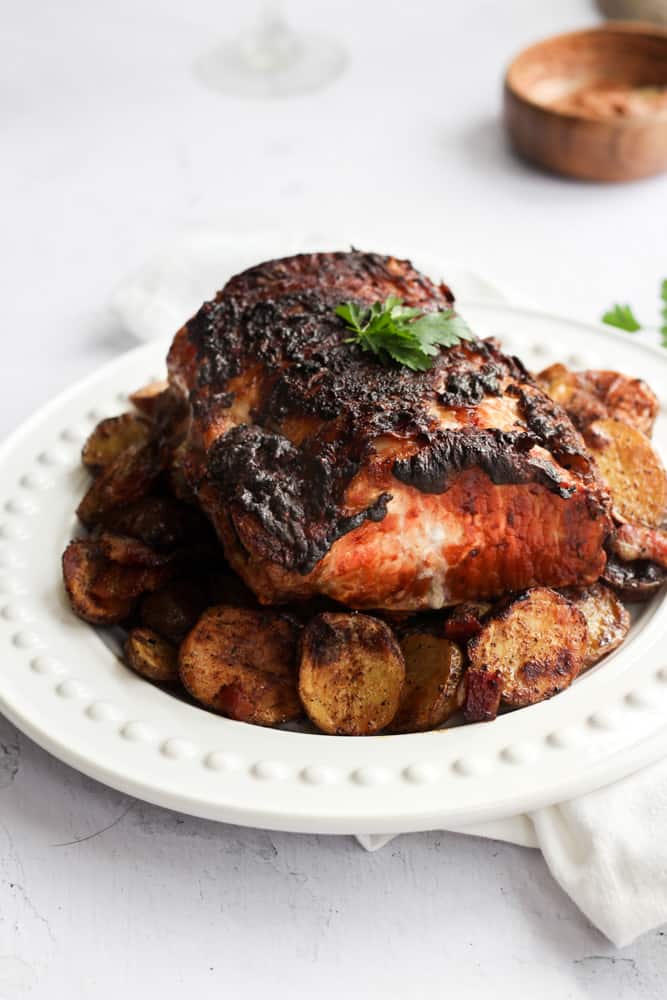 a roast that was cooked in the air fryer with a crispy, dark skin served on a white platter over a bed of halved baby potatoes