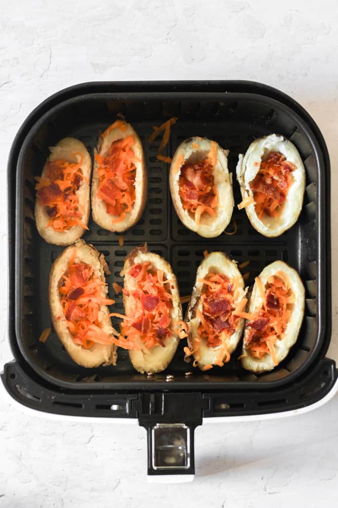 potato skins topped with cheese and bacon in an air fryer basket