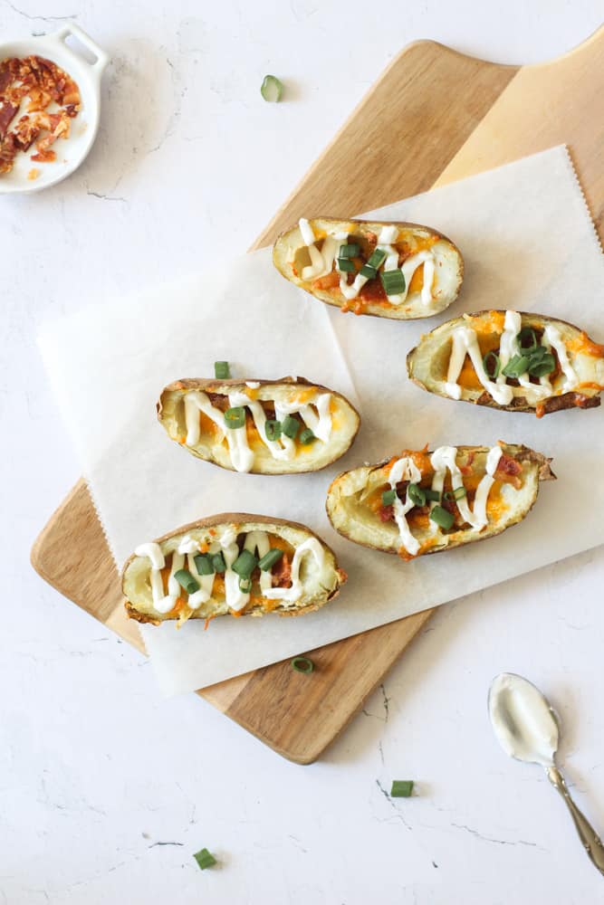 easy air fryer potato skins topped with sour cream on parchment paper on a wood board resting on a white backdrop