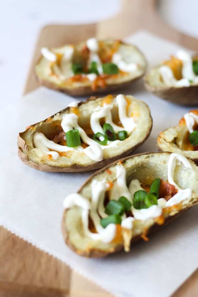 close up of an air fryer potato skin topped with sour cream and green onion on a piece of parchment paper