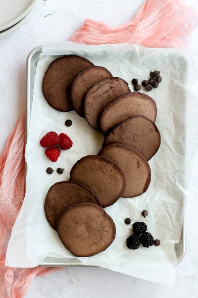 healthy vegan chocolate pancakes in an S shape on a piece of parchment paper on top of a pink napkin