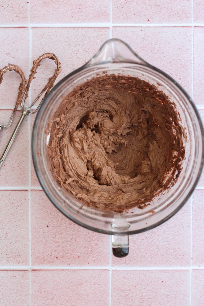 quick and easy chocolate buttercream in a clear glass bowl on a pink backdrop