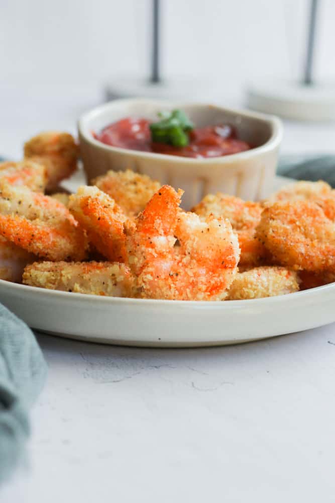 gluten free fried shrimp on a white plate featuring one standing on edge in front of a mound of air fryer shrimp