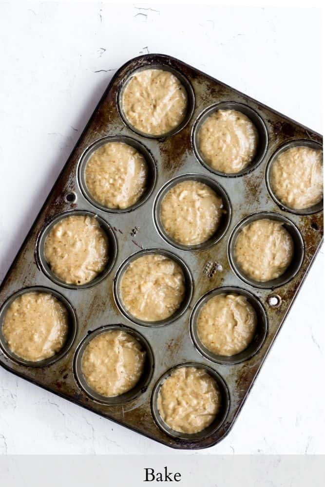 healthy banana bread muffin batter getting ready to bake in a dark gray muffin tin on a white backdrop