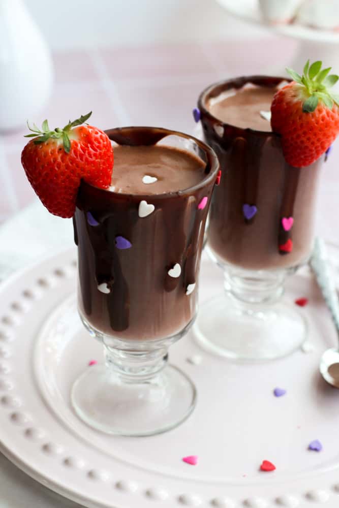two decorated clear mugs topped with cut strawberries filled with healthy strawberry hot chocolate
