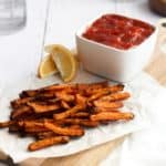 air fryer carrot fries on parchment paper with a bowl of ketchup on a white backdrop