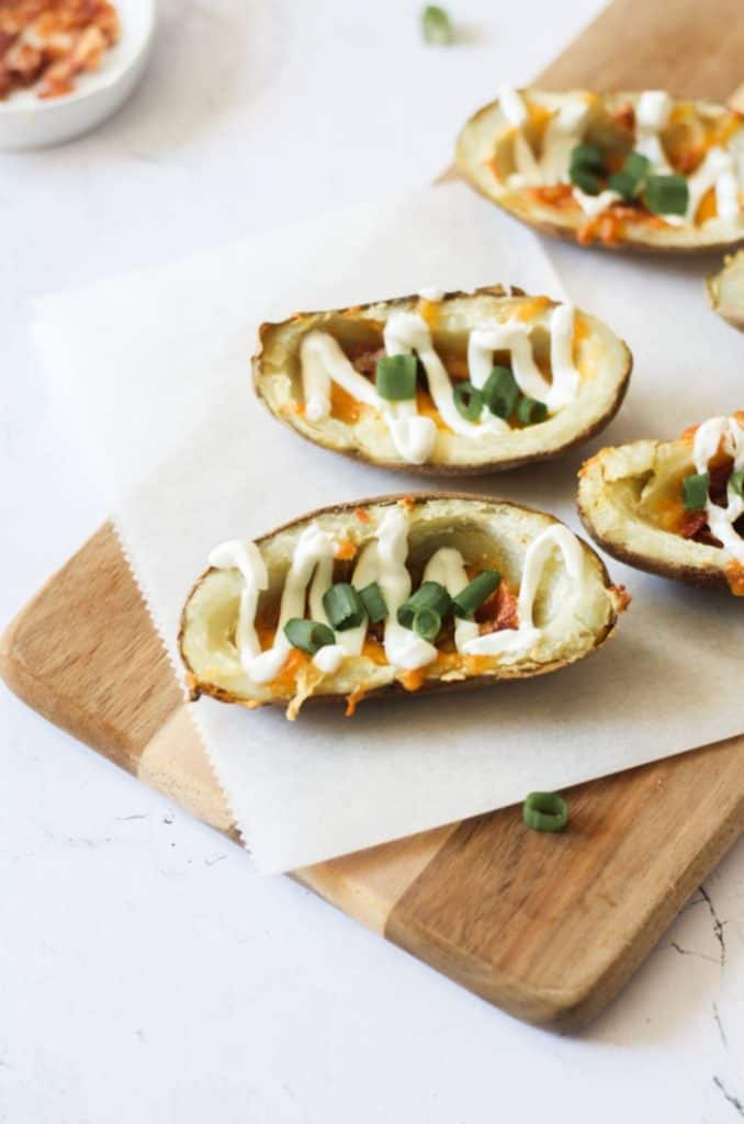 air fryer potato skins topped with sour cream and green onions on parchment paper on a wood board