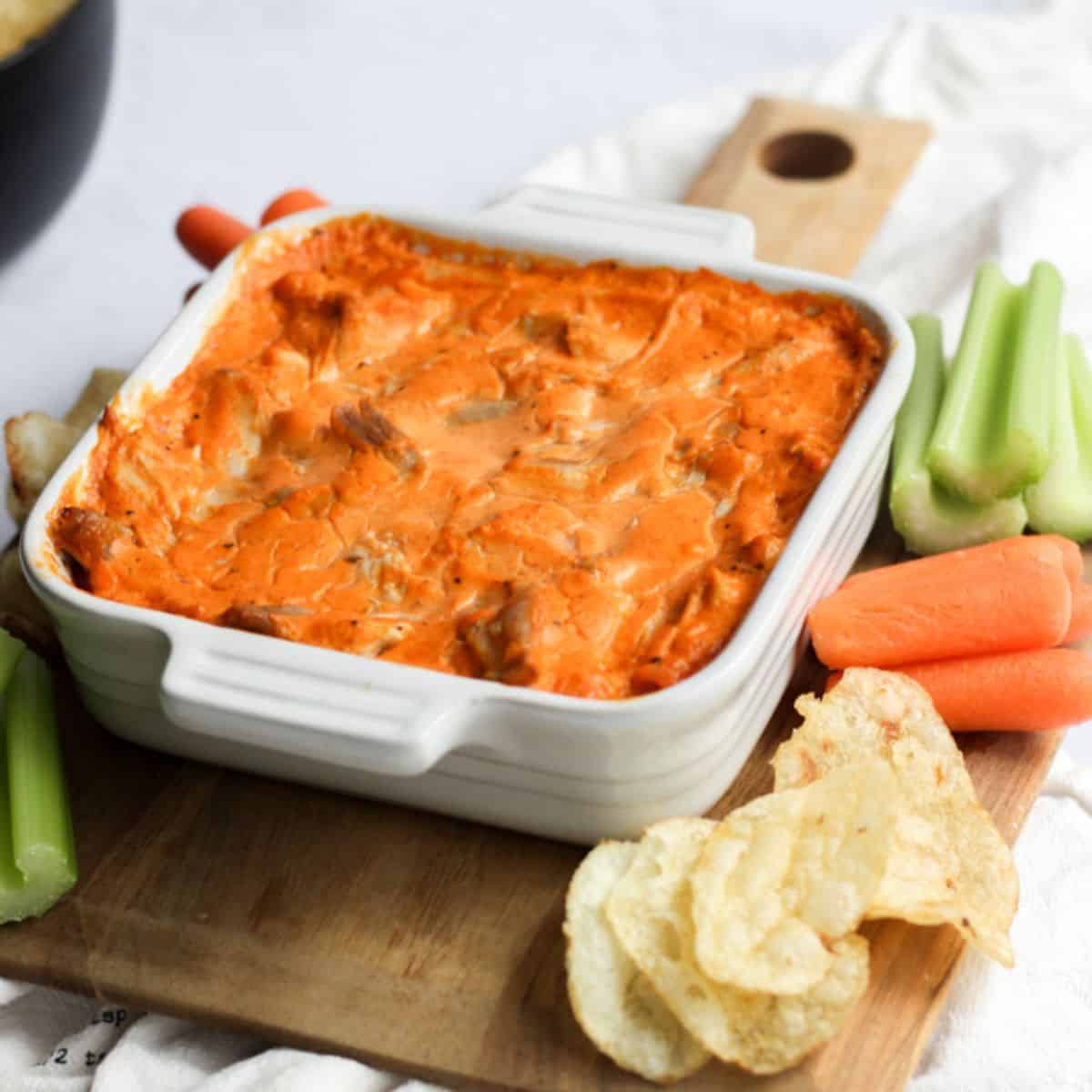 dairy free buffalo chicken dip in a white baking dish surrounded by carrots, celery, and potato chips.