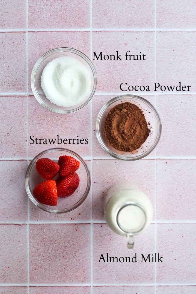 healthy strawberry hot chocolate ingredients on a pink backdrop labeled with black text