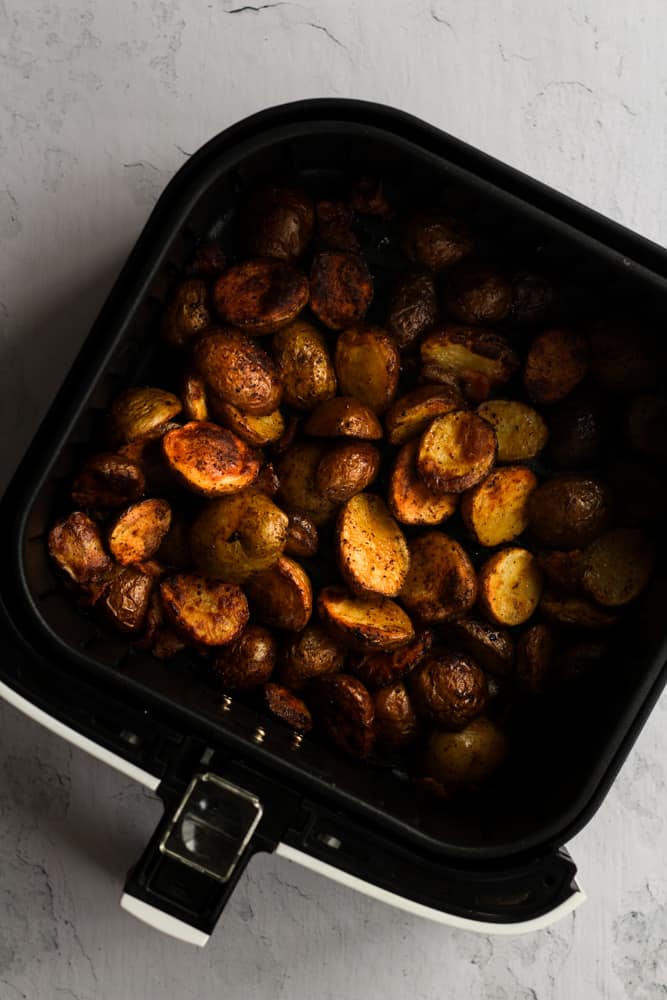 Cooked baby potatoes and bacon in the basket of an air fryer