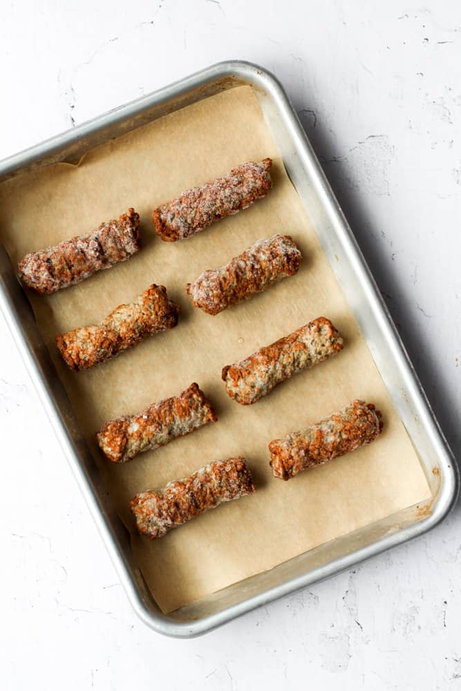 sausage links on a brown parchment paper lined baking sheet.