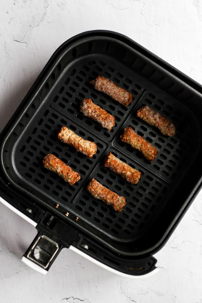 frozen sausage links in a black air fryer basket.