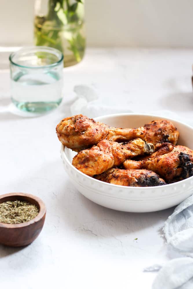 crispy chicken legs in a white bowl with a glass and a bowl of seasoning.