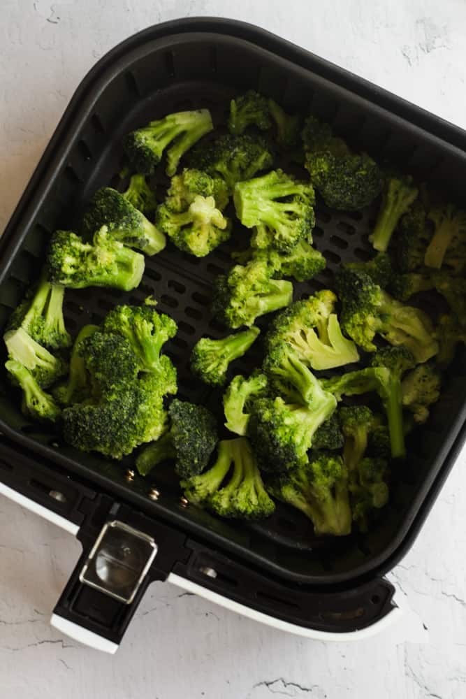 frozen broccoli in black air fryer basket.
