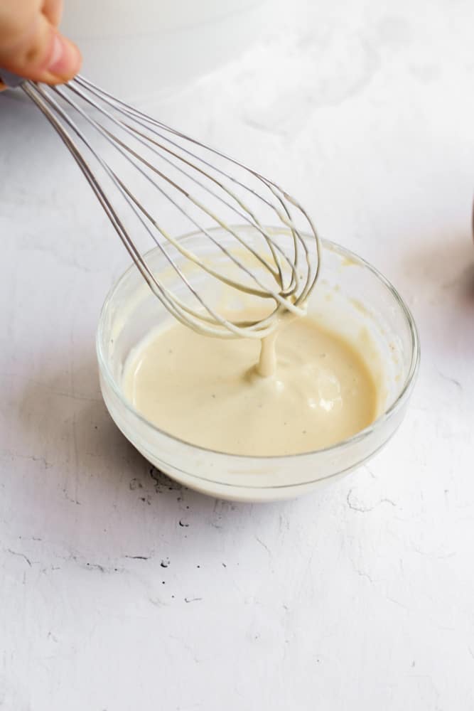 tahini sauce in small clear bowl with a silver whisk.