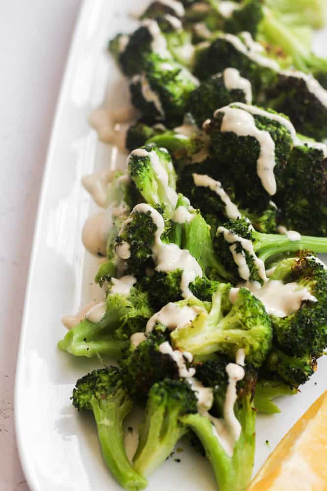 air fryer frozen broccoli with tahini sauce on white platter.