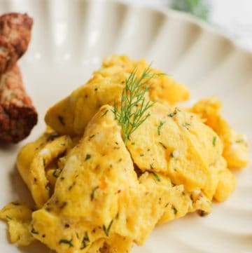 healthy scrambled eggs without milk on a white plate topped with a sprig of dill.