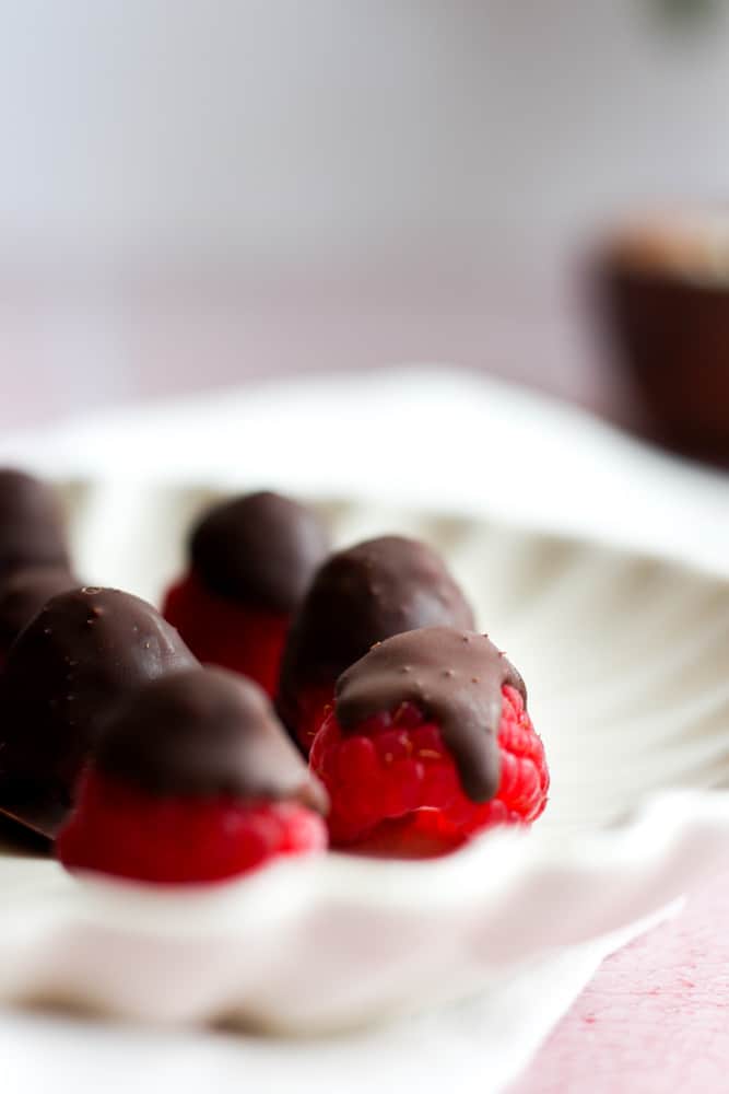 dark chocolate raspberries on a white scalloped edge plate.