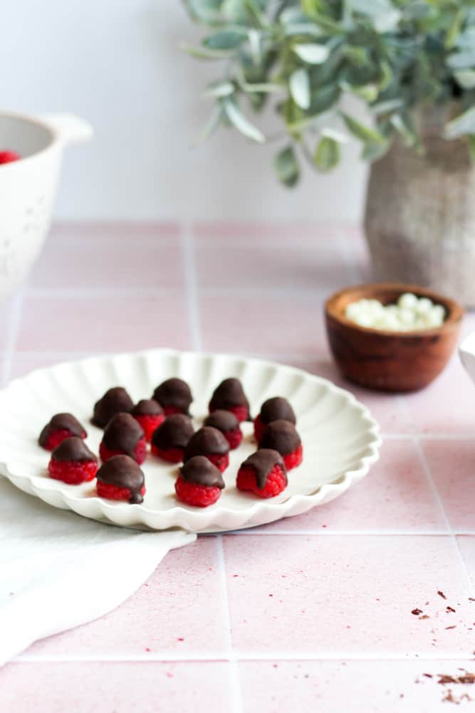 dark chocolate raspberries on a white plate on a pink backdrop with a white napkin.