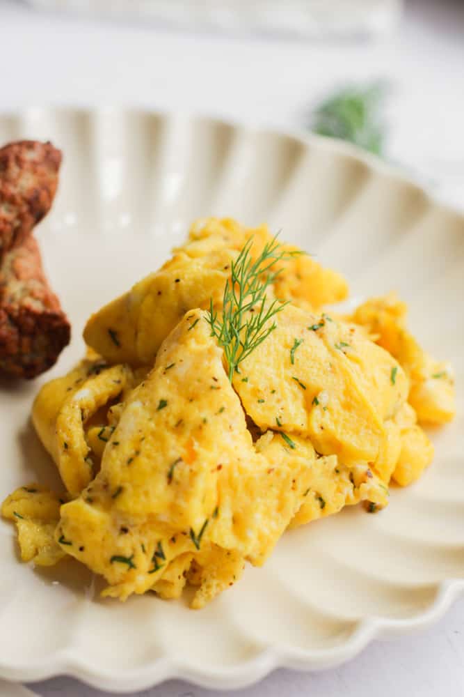 healthy scrambled eggs without milk on a white plate topped with a sprig of dill.