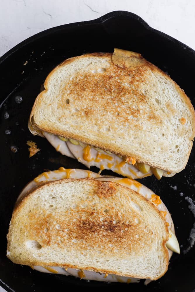 two sourdough sandwiches cooking in a cast iron skillet. 