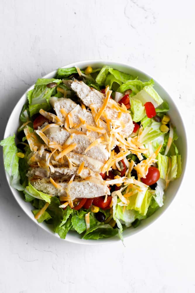 salad with corn, black beans, tomatoes, and chicken topped with shredded cheese.