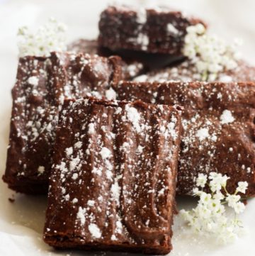 dairy free brownies with powdered sugar on a white plate with baby's breath flowers.