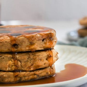 three oat flour pancakes on a white plate with syrup dripping down the sides.