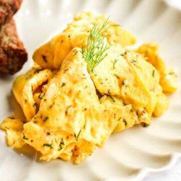 dairy free scrambled eggs on a white plate with fresh dill on top.
