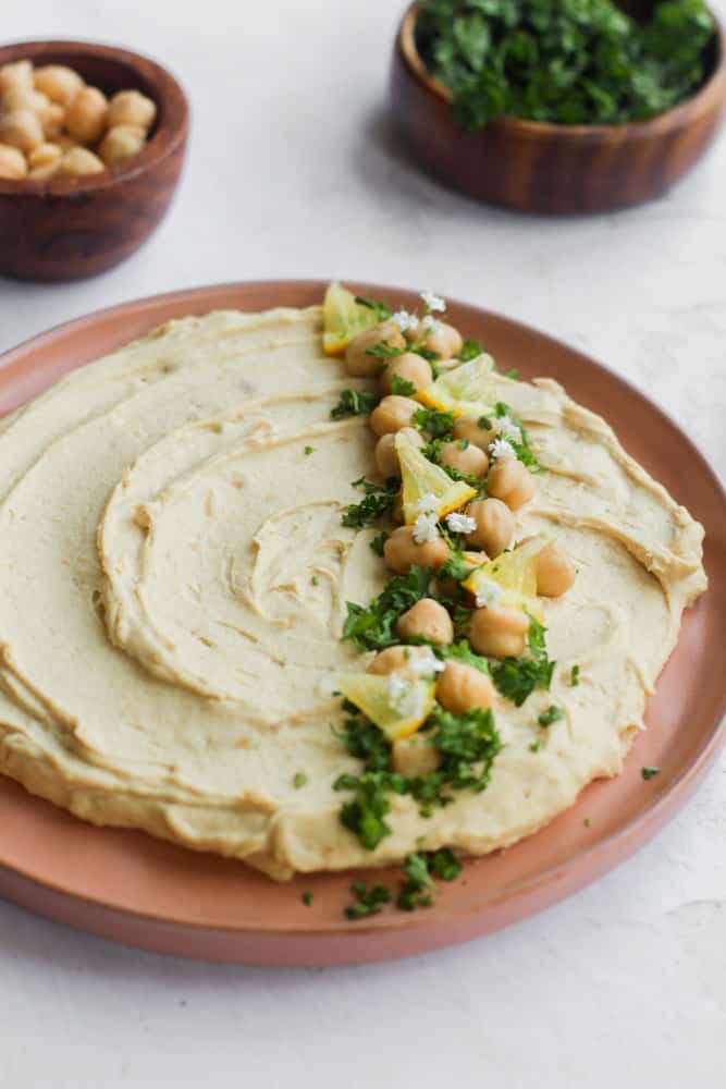 oil free hummus topped with chopped herbs on a tan plate.
