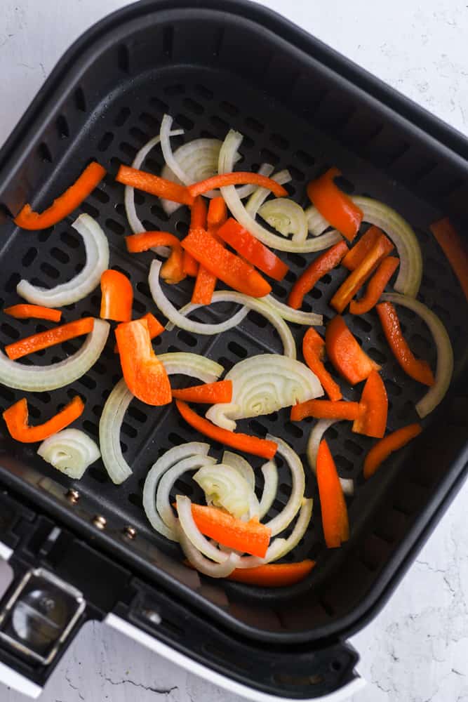 onions and orange bell peppers in air fryer basket.