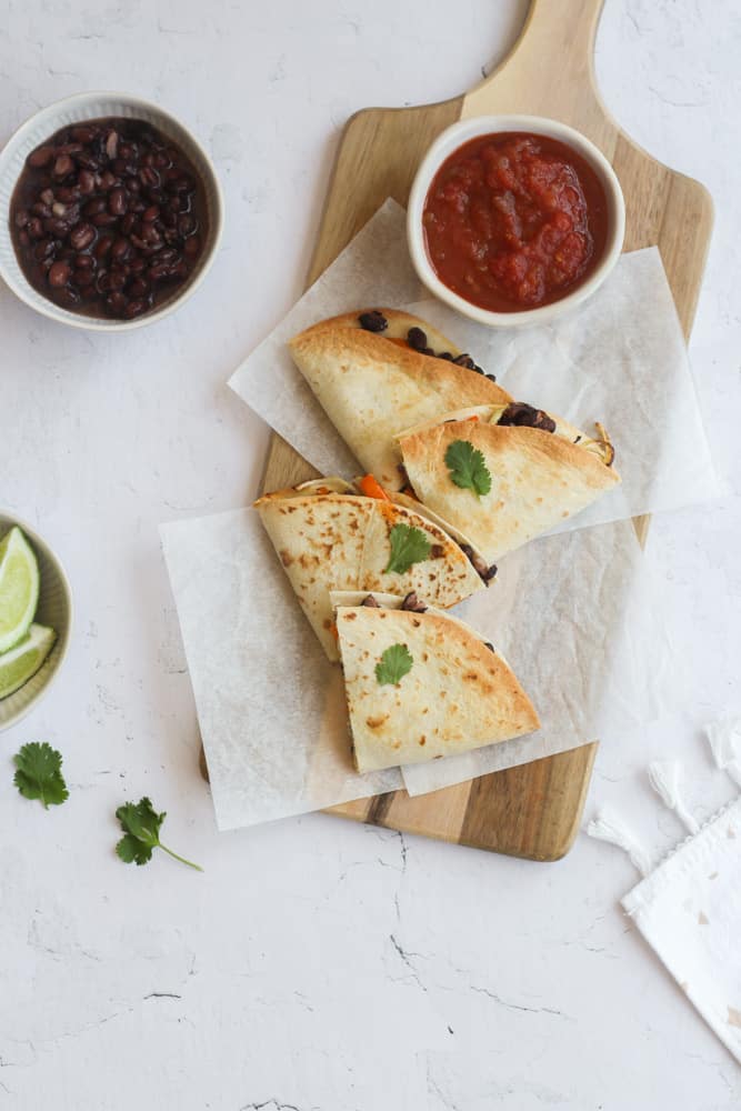 vegan air fryer quesadilla cut into triangles on a wood board with salsa.