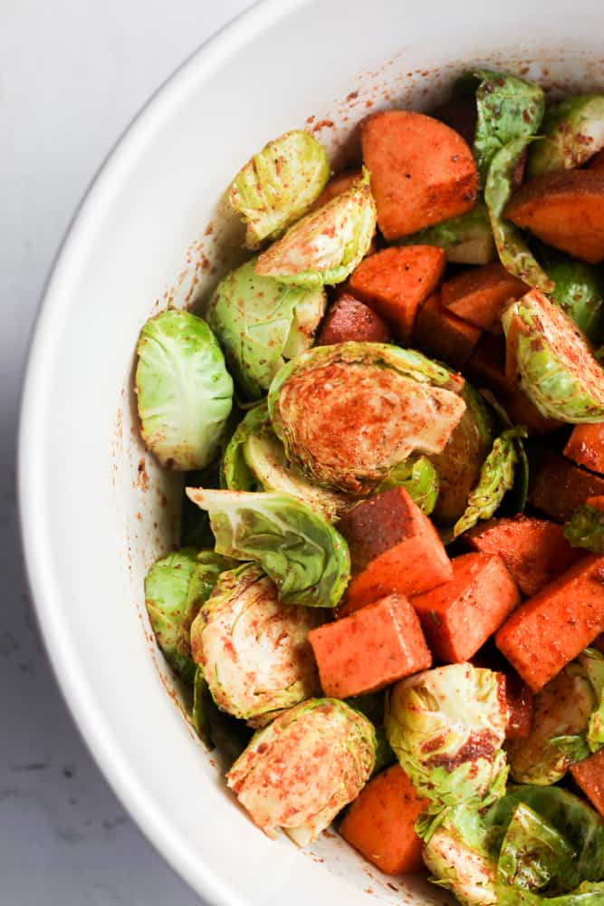chopped brussels sprouts and sweet potatoes in a white bowl with seasonings.