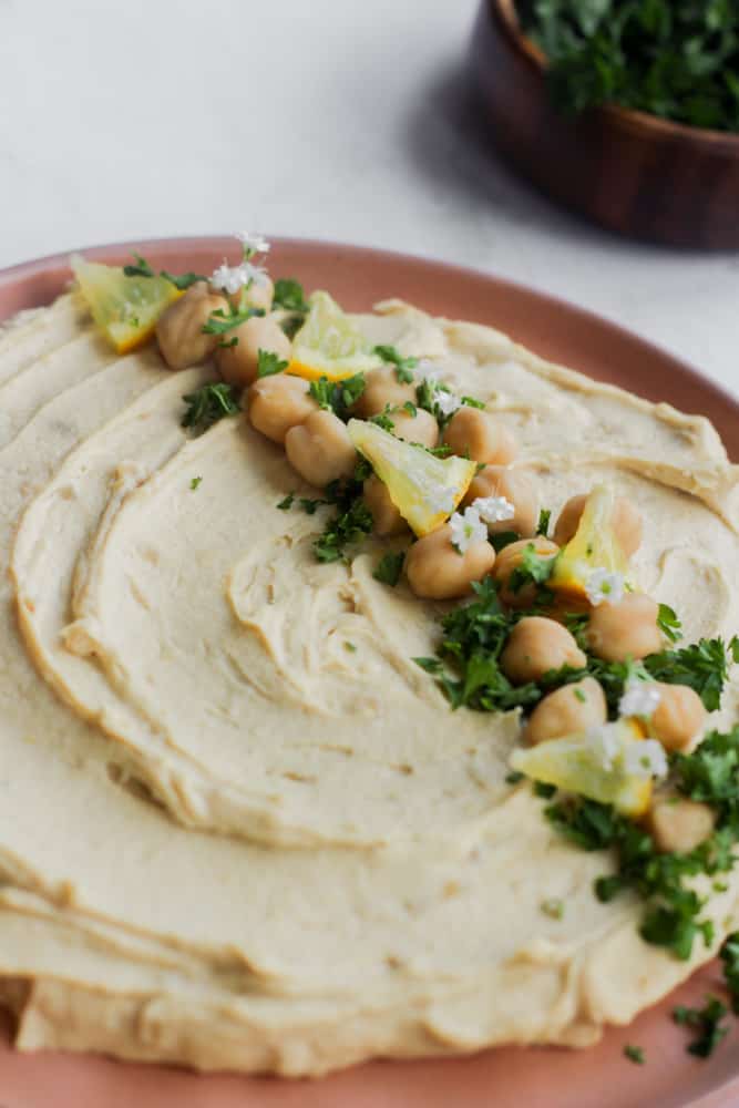 quick oil free hummus topped with chickpeas and chopped herbs on a rose colored plate.