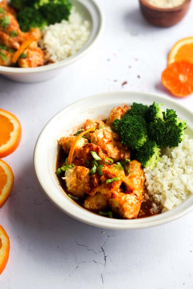 air fryer paleo orange chicken recipe served in white bowls with rice and broccoli.